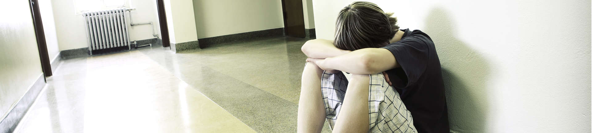 Depressed teenager with head down sitting by the wall and hiding face in his arms