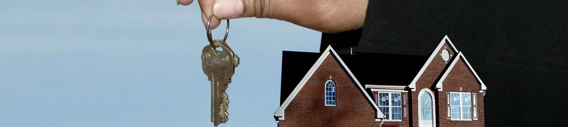 Person holding house keys in one hand and showing a mini model of a house