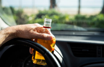 driver driving a car with a bottle of alcohol in his hands
