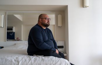 Frustrated overweight man sits on bed sadly looking to window feeling depression from difficult relations, works trouble, health problem. Unhappy male think about hopelessness need psychological help